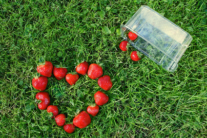 strawberries dumped out of container into grass, forming a heart