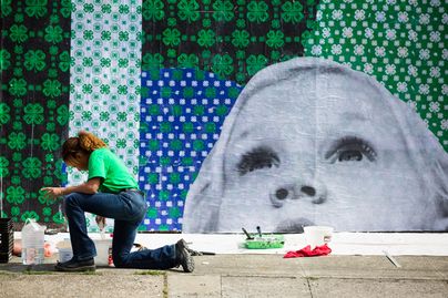 youth kneeling with art supplies in front of a mural of 4-H clovers and a face of a little kid