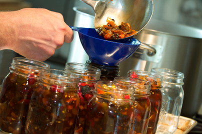 pouring food into glass jars to prepare for canning