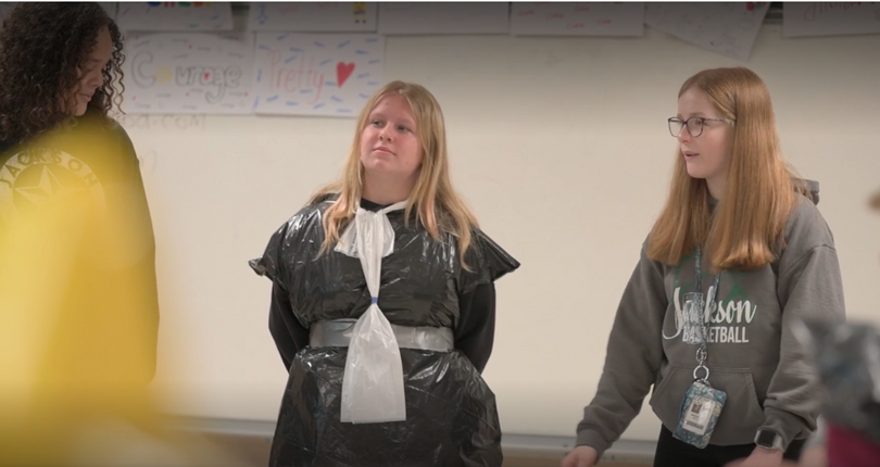 Three middle school aged girls make professional dress out of garbage bags and found objects.