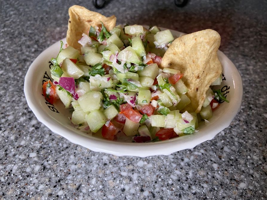 Prepared cucumber salsa in a bowl with two tortilla scoops dipping into the bowl. 