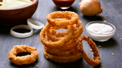 stack of onion rings with a bowl of dip in the background