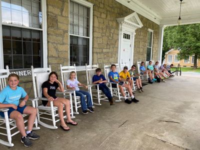 Young 4-H'ers sitting in white rocking chairs lined up on the front porch of Jackson's Mill's dinning hall