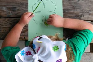 4-H Cloverbud with bow in hair painting a green paper with clover outline