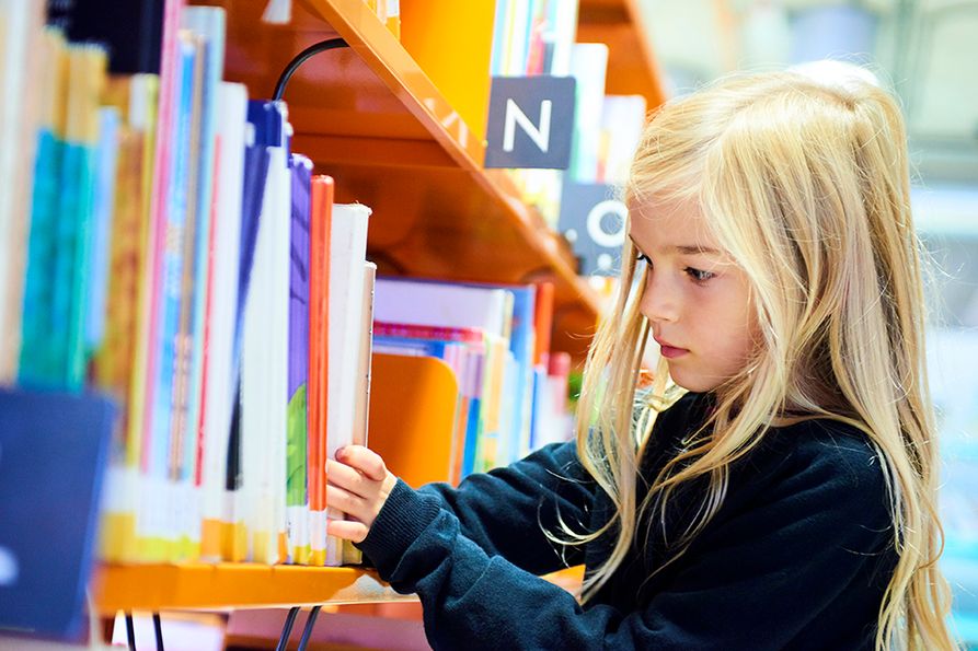young girl choosing a book from the library shelf