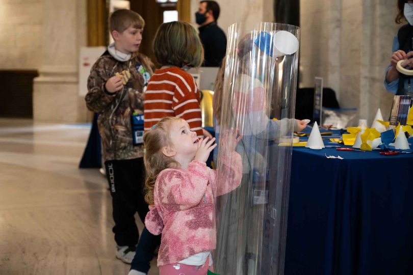 A young girl watches her flying machine float up into the wind tunnel during a STEM activity.