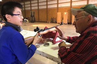 4-H Youth being assisted by adult with air rifle instruction