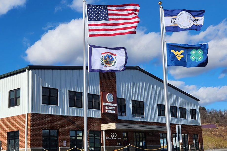 The American flag, West Virginia flag, Monongalia County flag, and WVU 4-H flag fly in front of the WVU Extension Monongalia County office.