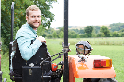 young male farmer on an orange tractor turning around to face camera smiling
