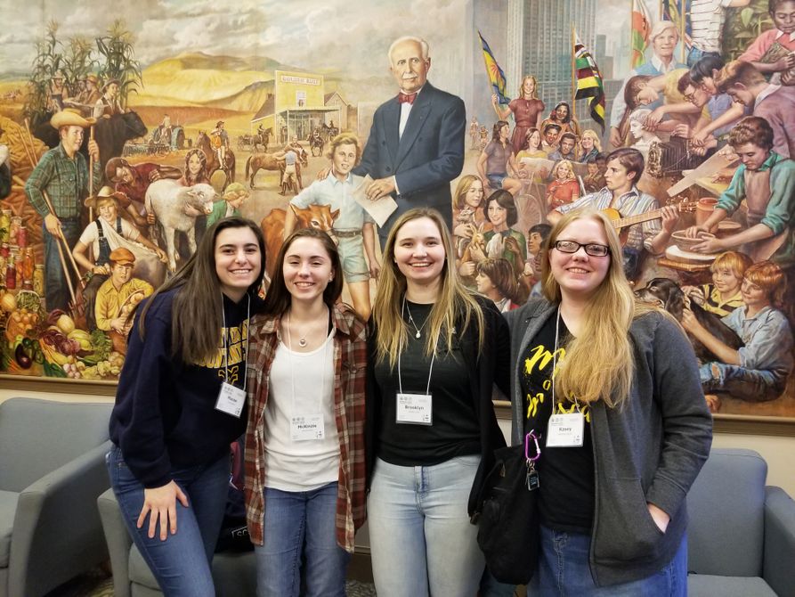 Four youth 4-H girls stand in front of a painting at the National 4-H Conference Center