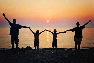 Two adults and two children holding hands in the dark with a body of water and sunset behind them