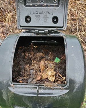 A compost tumbler with leaves in the bin.
