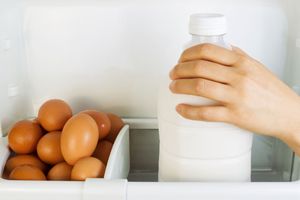 A person selects a jar of milk from the fridge with eggs in a carton.