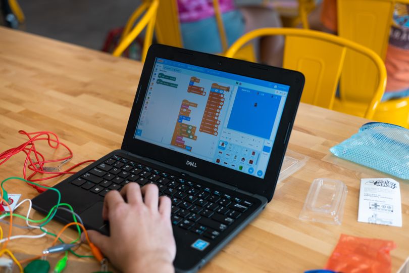 Laptop showing Scratch coding platform with a kid's hand at the mouse.