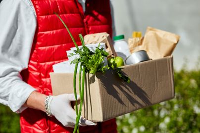 A man in a vest jacket delivers a box of food and supplies while wearing gloves.