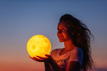 A young woman holds the full moon in her hands.