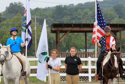 Two youth on horses holding flags and two youth standing on ground with a flag.