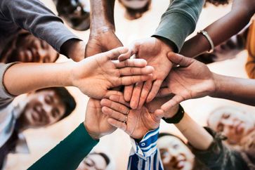 A group of people forming a team put their hands together. Smiling faces around.