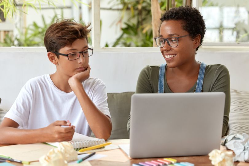 Woman smiles at teenager as they work together while looking at a laptop. 