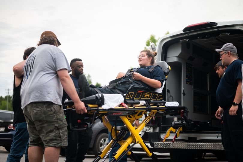 Woman on a gurney being loaded into an ambulance by a few men at an EMT training course.
