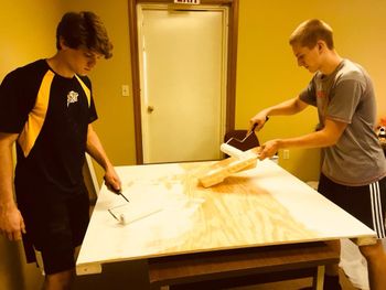 two teen boys paint the foundation color onto plywood