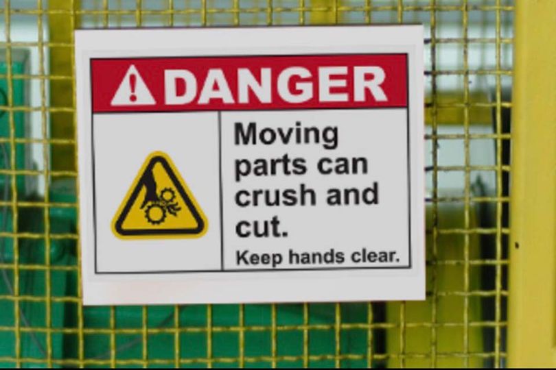 Signage on machinery that reads "Danger. Moving parts can crush and cut. Keep hands clear."