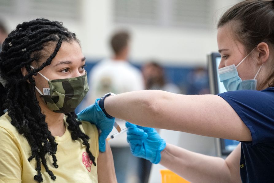 A young woman wearing a camo mask receives a vaccine shot.
