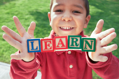 young boy holding blocks with letters on them spelling out the word "learn"