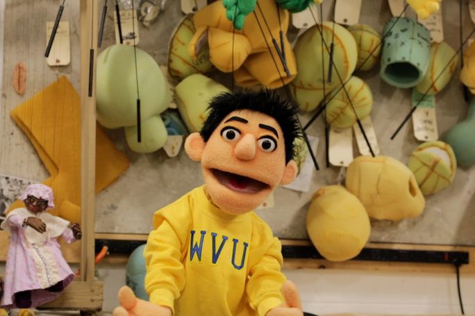 A male puppet in a gold sweatshirt with the letters "WVU" on it.
