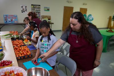 Kids cutting tomatoes in a kitchen with help from adult