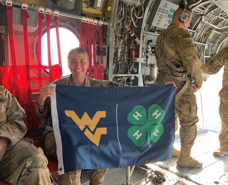 Andrea Gump holds Ohio County's WVU 4-H flag in U.S. Army aircraft in Kuwait.