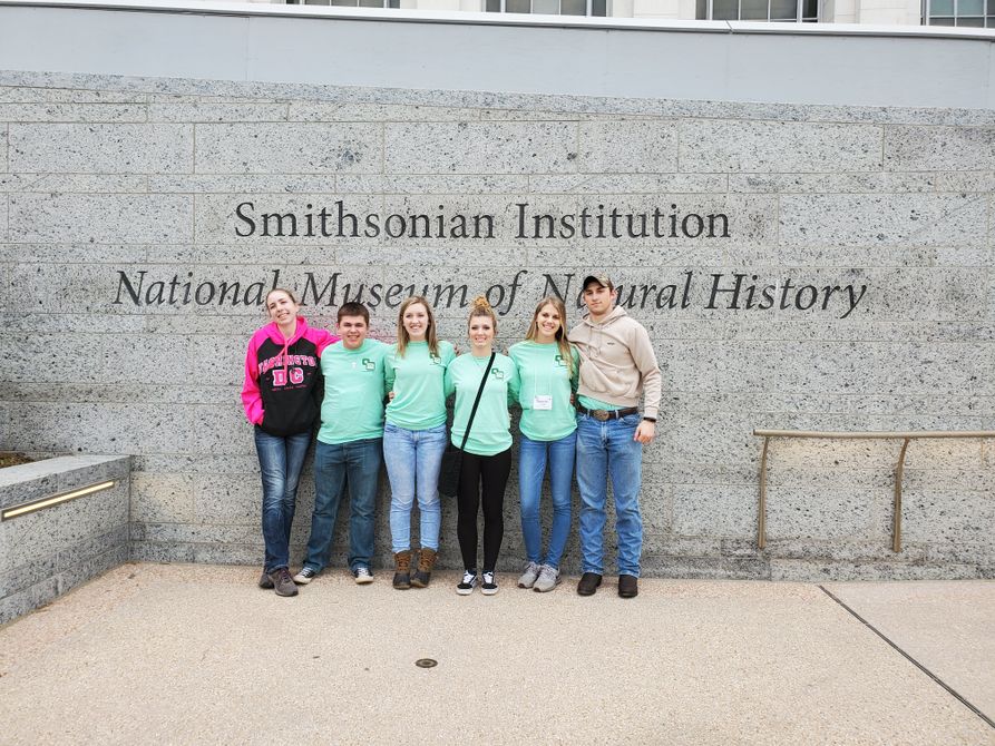 Six youth stand for a group photo in front of a wall that has "Smithsonian Institution, National Museum of Natural History"