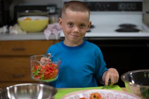 Boy in kitchen with a measuring cup of tomatoes, bowls, cutting board, and knife