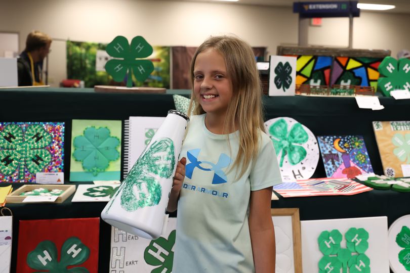 Young girl holds a 4-H megaphone in front of shelves full of 4-H projects.