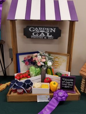 Display stand with roof for the Garden Gal Veggies and Art business. Stand holds an arrangement of flowers, assortment of vegetables, jam jars, soaps, and two frames pictures.