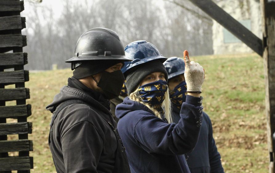 Two people wearing hard hats and face masks discuss a building structure