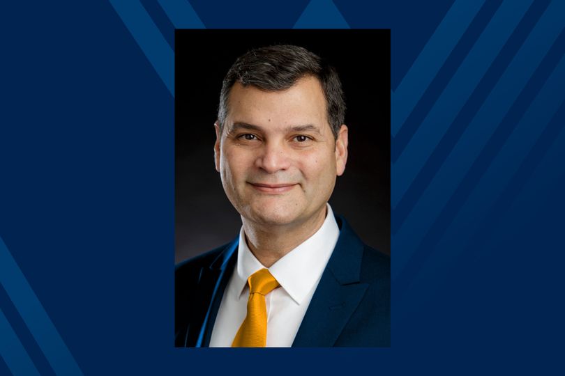 Navy blue background with a photo of Jorge Atiles in a blue suit and gold tie