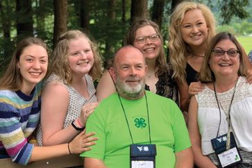 An adult volunteer surrounded by 4-H'ers.