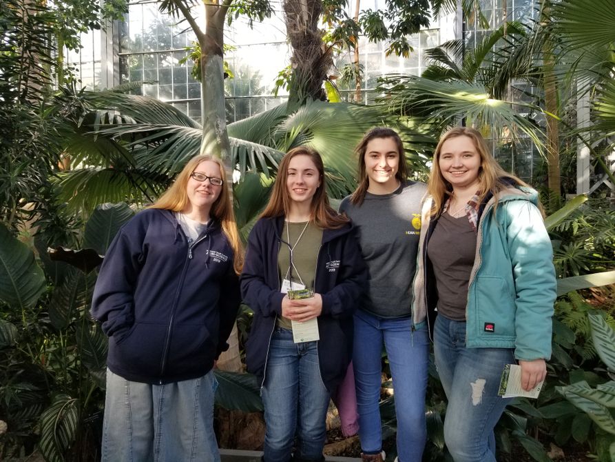 Four youth 4-H girls stand on an overlook at the U.S. botanical gardens surrounded by diverse plant life.