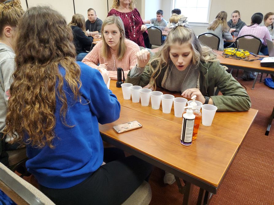 Four female youths file clear plastic cups with beads to simulate the exponential growth of germs.