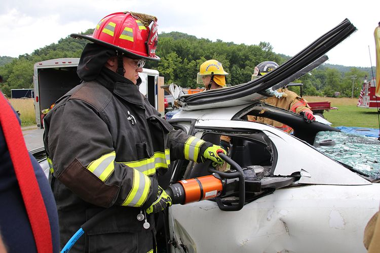 Jr Firefighter in gear uses tools to disassemble a car for a rescue