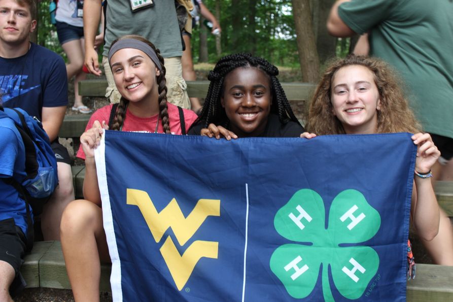 Three girls holding a West Virginia University and 4-H clover flag at a state camp.