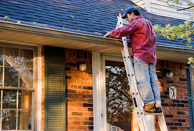 man on ladder cleaning house gutters