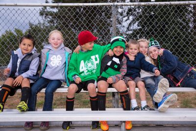 Six elementary youth sitting on bleachers with arms around eachother