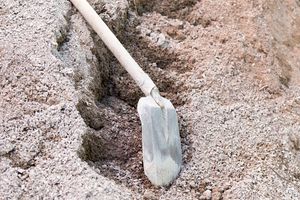 A shovel rests on the ground in a dirt trough.