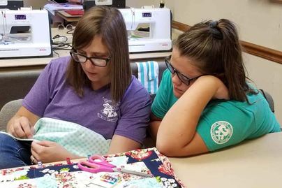 Adult and youth learning how to stitch the binding of a quilt