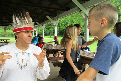 Young camper talking to Native American cultural expert in traditional headdress 