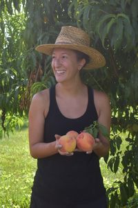 Female peach grower holding peaches in front of tree.