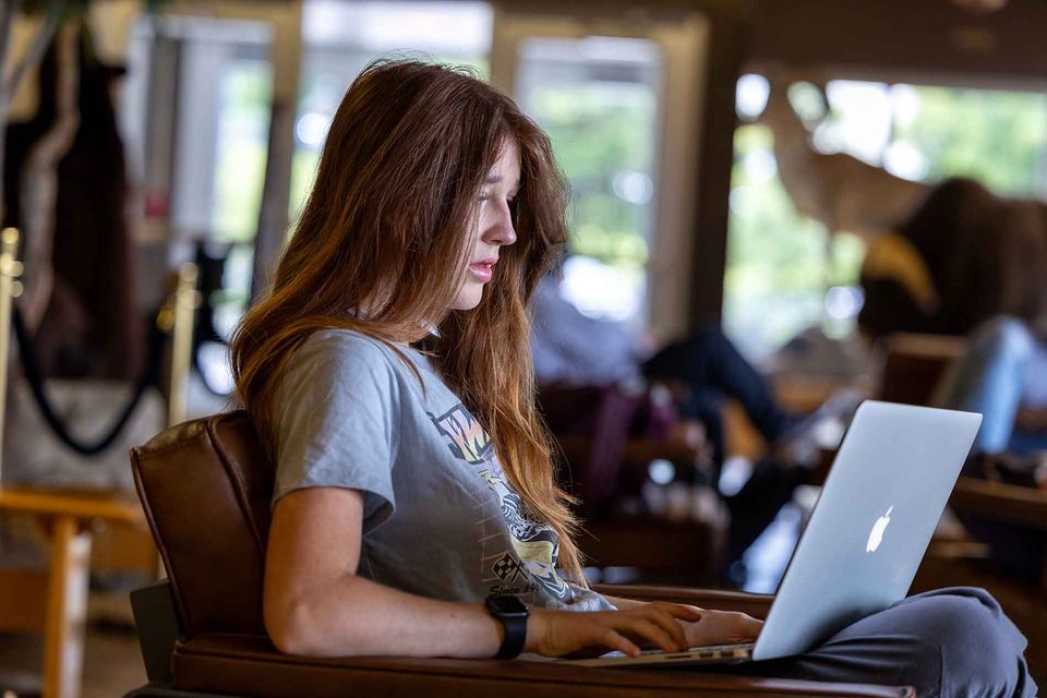 A female student sits in a lounge working on her computer