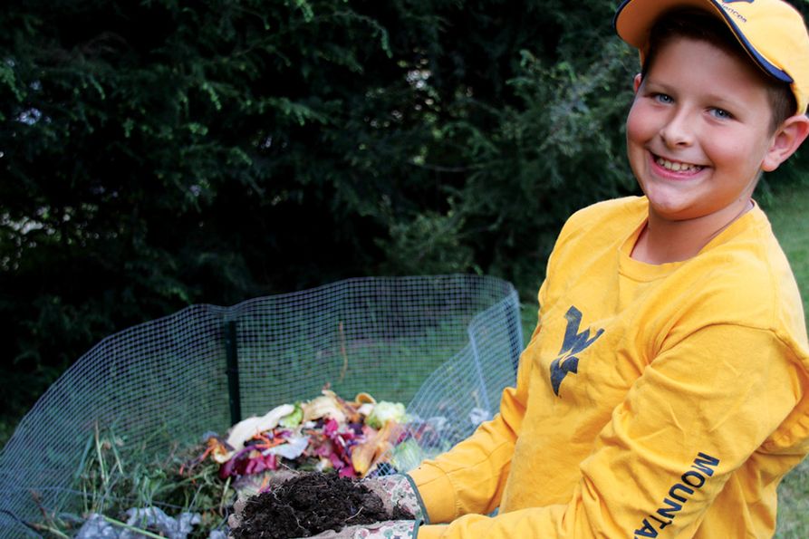 The cover of WVU Extension's 2019 Garden Calendar features a boy in Mountaineer gear wearing gloves and holding fresh compost. The cover reads Back to Garden Basics.
